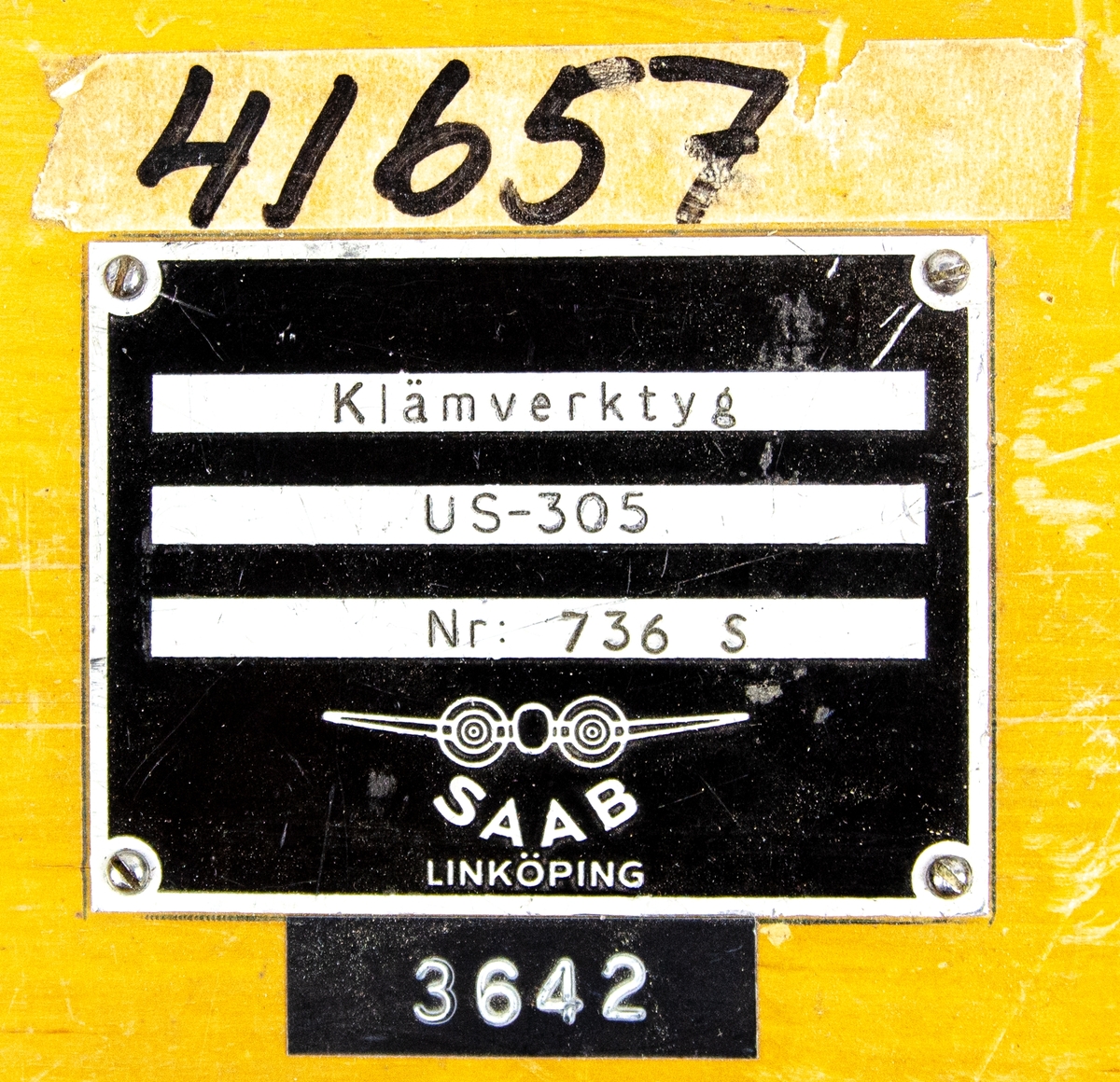 Klämverkty, förvarad i tillhörande originallåda av trä. På ovansidan av lådan finns en SAAB-skylt med texten: "Klämverktyg US-305 Nr: 736 S". Ovanför skylten finns siffrorna "41657" skrivet på en tejp och under skylten står det "3642". På framsidan finns en annan skylt: "UNO SÄRNMARK AB GÖTEBORG US SWEDEN Typ US-305 A T:nr 119".