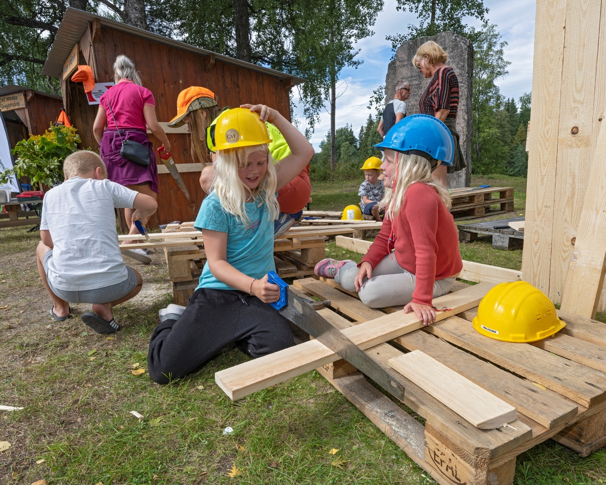 Barn bygger plankehytte på Skogbrukstunet under De nordiske jakt- og fiskedager 2022 på Norsk skogmuseum, Elverum, Innlandet. Plankehytta. To jenter er ivrig opptatt med saging.
