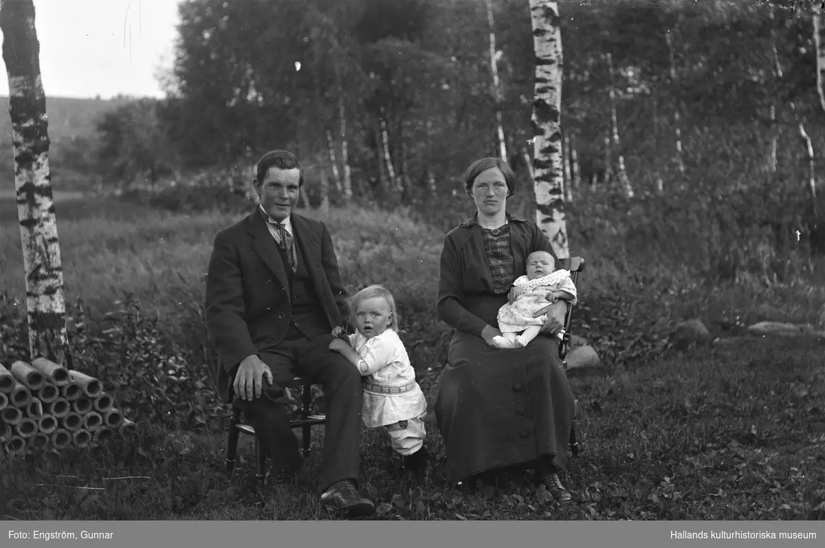 Ett ungt par, Klas och Linnea Andersson, sitter med sina små barn utomhus vid ett par björkar på Klingeberg, Hästhagen (Danskens) i Sällstorp. Pojken vid Klas heter Gunnar Sigurd och bebisens namn är Elin Viola, född i juli 1916, så det ger bildens datering. Till vänster ligger smala rör travade. (Se även bildnr GEA006)