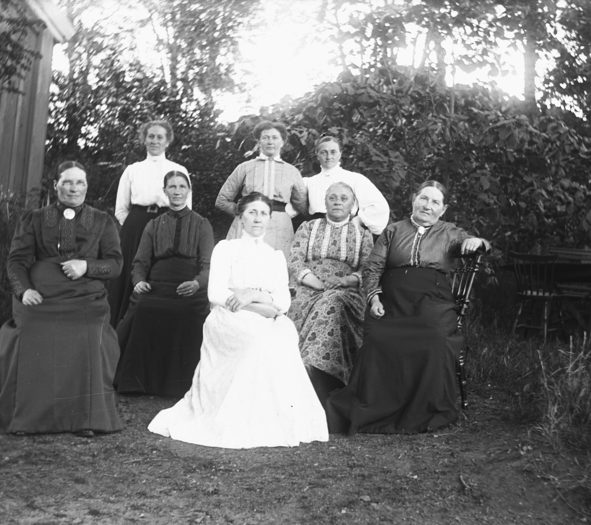 Systrarna Engström tillsammans med en grupp äldre kvinnor i en trädgård. Constance sitter med mönstrad klänning näst längst till höger med Bertha stående bakom och Fredrika sittande framför.
(Bild 1 är beskuren)