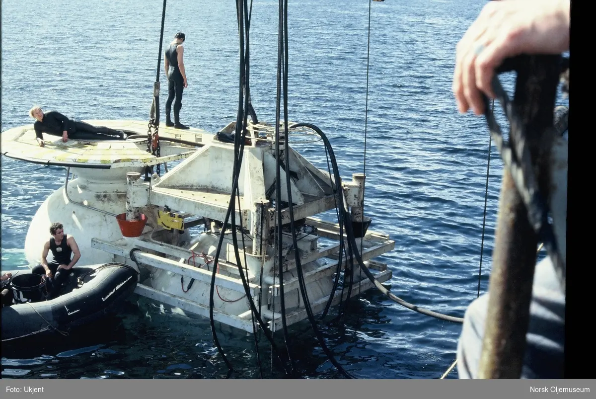 Moduler for et undervannsanlegg monteres utenfor kanten fra en båt eller lekter. Menn i våtdrakt arbeider oppå modulene.