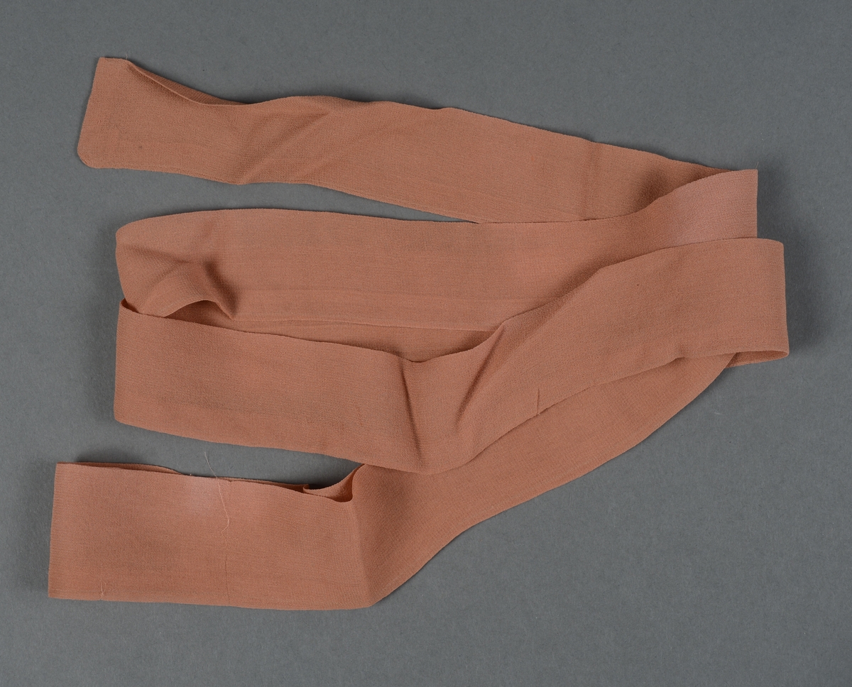 Belte sydd av silkekrepp, mellombrunt. Sydd sammen for hånd av to lengder ellers vrangsydd på maskin. Trolig brukt utenpå kjole eller drakt.