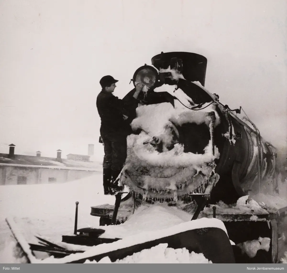 Damplokomotiv type 39a på Finse stasjon. Fyrbøteren fjerner is og snø fra frontlykten