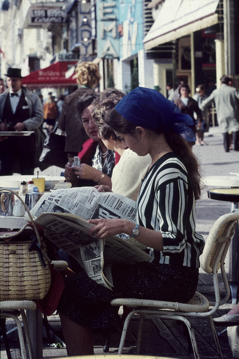 Foto av en ung kvinne som leser avisa ved et kafebord.