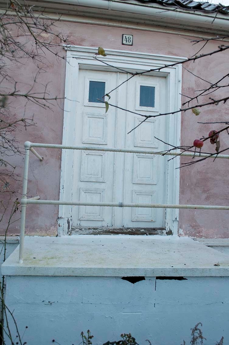 Vitmålad entrédörr, en trappa upp, till rosaputsat envåningshus. Ovanför dörren en liten skylt "48".