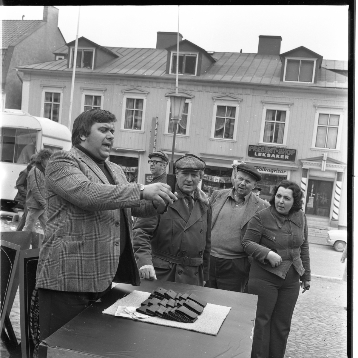 En man i kavaj står vid ett bord och säljer troligen plånböcker. Vilbert Fredriksson, till vänster, med flera tittar intresserat.