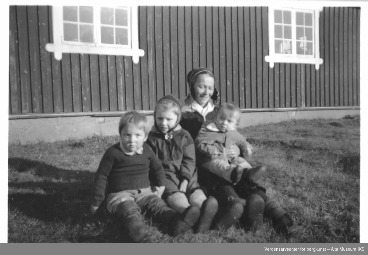 Kvinne og barn sitter på plenen utfor et hus.
