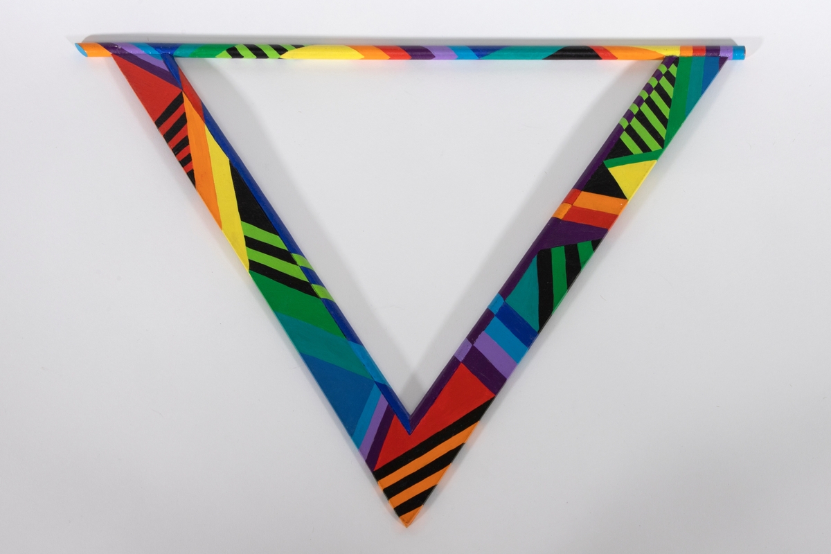 Skulpturelt halssmykke i trekantform satt sammen av en treplate og trepinner. Treelementene er malt i flere farger i geometriske mønstre. Smykket tres over hodet.
