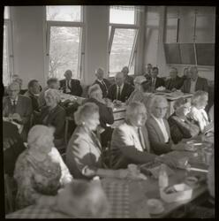 Fotografi av mange eldre menn og kvinner som sitter ved lang