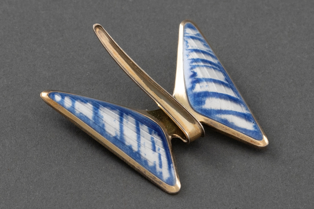 Brosjen er utformet som en sommerfugl. Kroppen ar av forgylt sterling sølv, mens vingene er av hvit og blå speilemalje. Et buemønster skimtes gjennom speilemaljen.