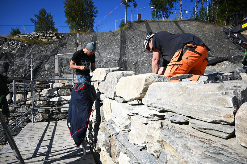 Bildet viser arbeidere som jobber med å bygge opp en større mur. I bakgrunnen ser man et steinbrudd og blå himmel. (Foto/Photo)