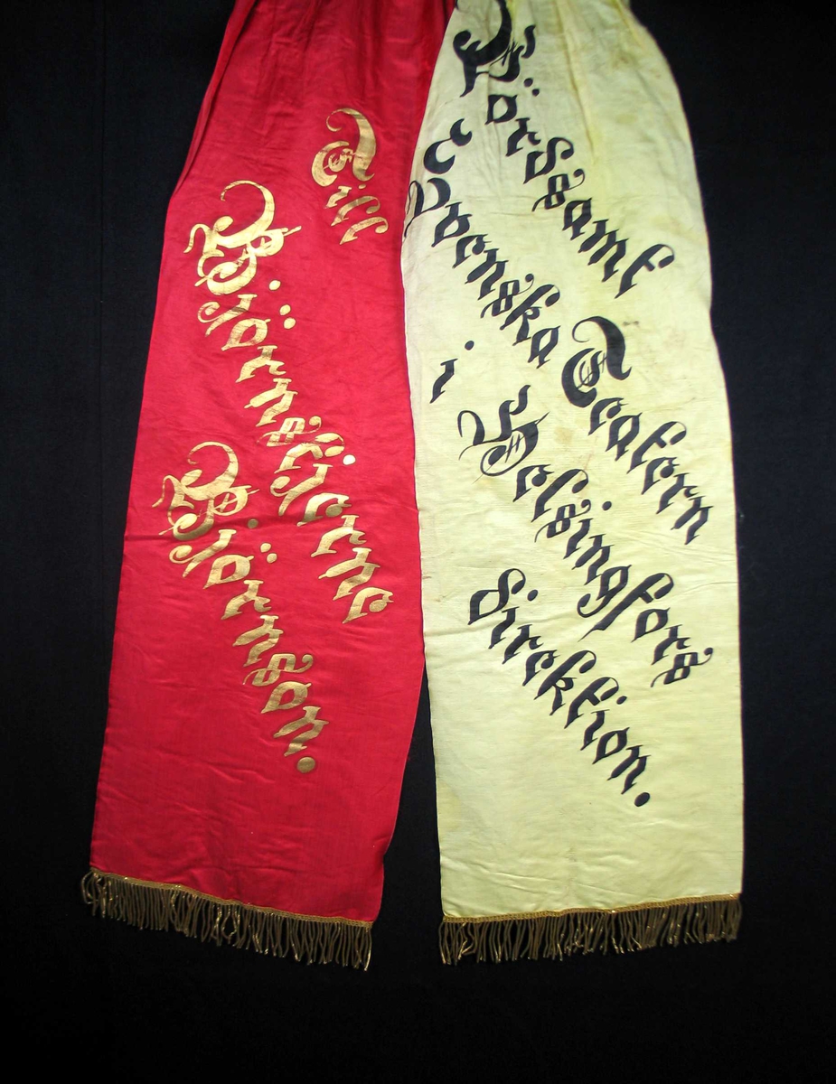 Begravelsessløyfe i rød og hvit silke med frynser og tekst i gull og svart.