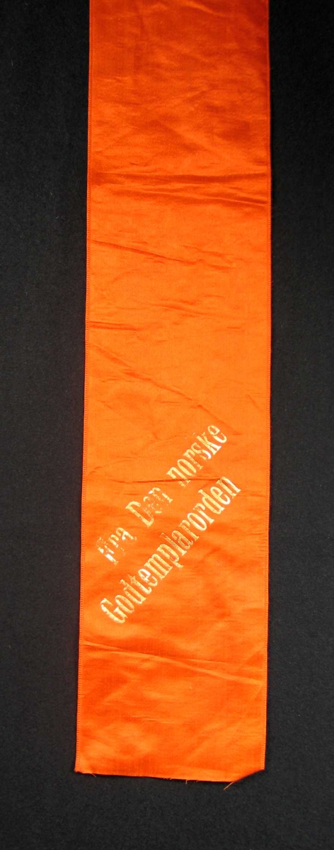 Begravelsessløyfe i oransje silke med tekst i gull.