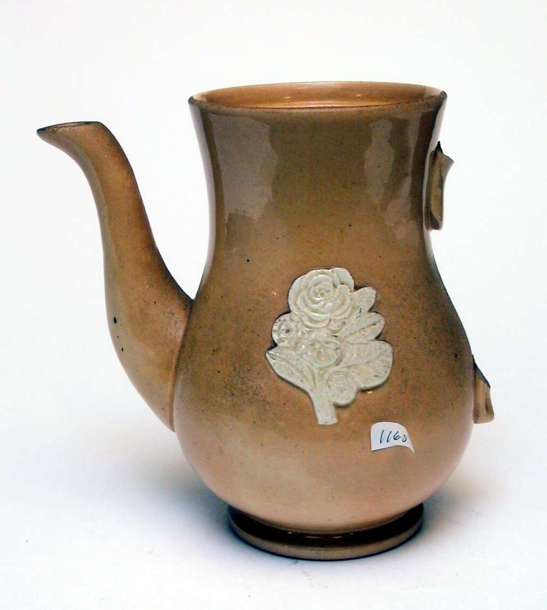 Kaffekanne av gul keramikk med påsatt blomsterdekor. Dekoren er elfenbenshvit. Lokket og hanken mangler.
Kannen har ingen produksjonsmerker. 