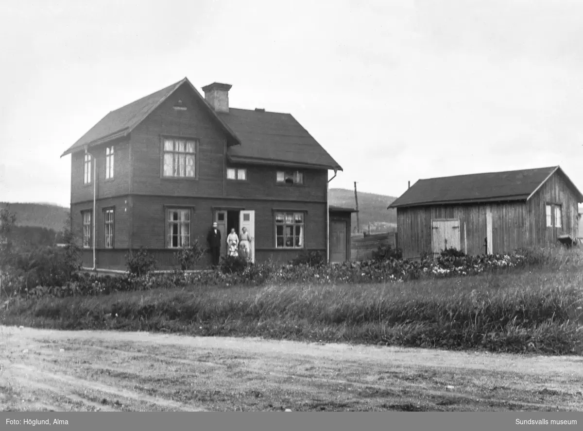Två bilder på sockenskrivare Daniel Höglunds fastighet som, innan den revs, låg i korsningen Fanbyvägen-Uslandsvägen. Första bilden tagen från Fanbyvägen. Vid ingången står en man, två kvinnor och två barn.