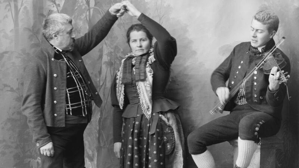 Dette er et gruppebilde der mann og kvinne ikledd Rørosdraktdanser pols. Felespiller sitter ved siden av.. Foto/Photo