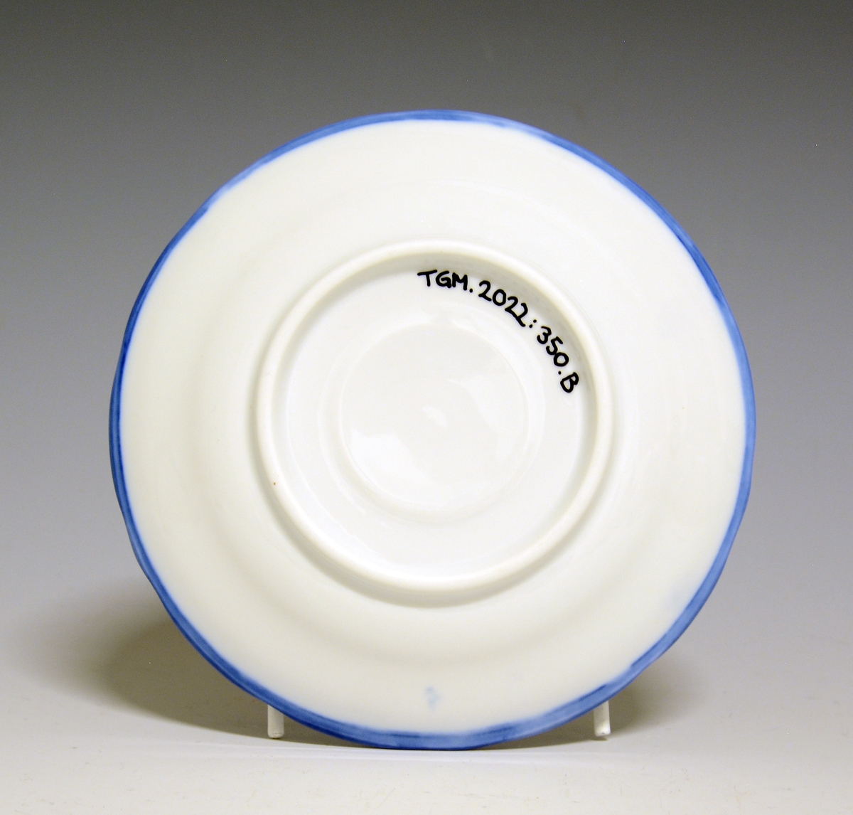 Kaffeskål av porselen. Hvit glasur. Håndmalt blå underglasurdekor på fanen, blå kantstrek ytterst.
Modell: Victoria, 1800
Uten fabrikkmerke.