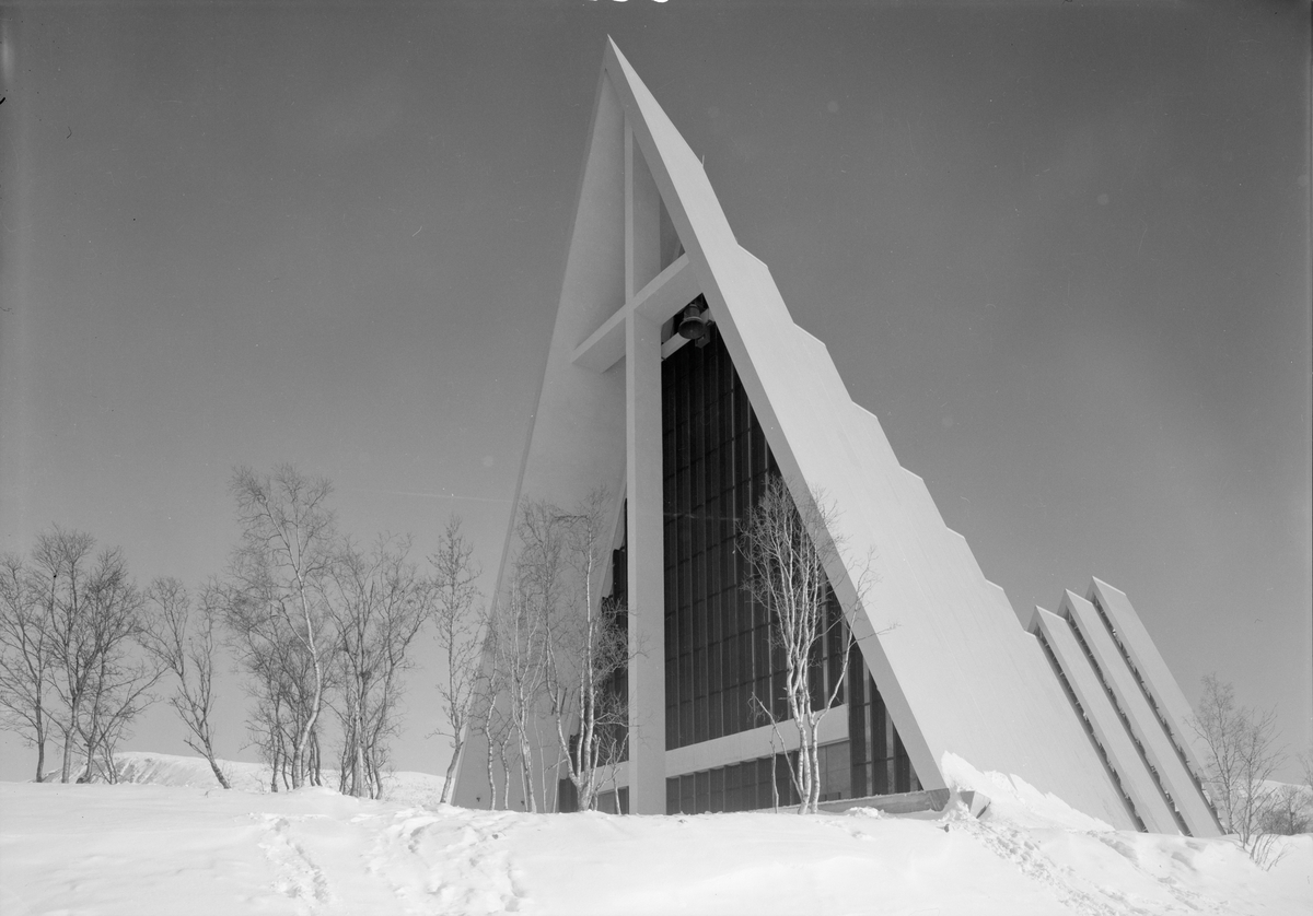Arkitekturfoto av Tromsdalen kirke, bedre kjent som Ishavskatedralen. Med sitt avtrappede båthusformede eksteriør og sine åpne glassgavler er den blitt et landemerke i området. Kirken ble innviet 19. november 1965.