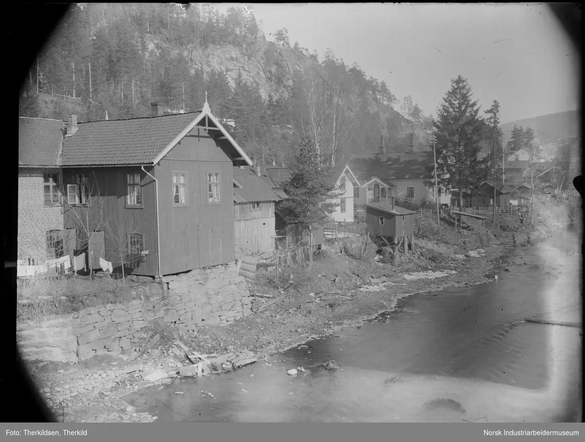 Rekke med bolighus langs elva i Tinnesgata, ved Tinnå bro. Klær henger til tørk utenfor ett av bolighusene.