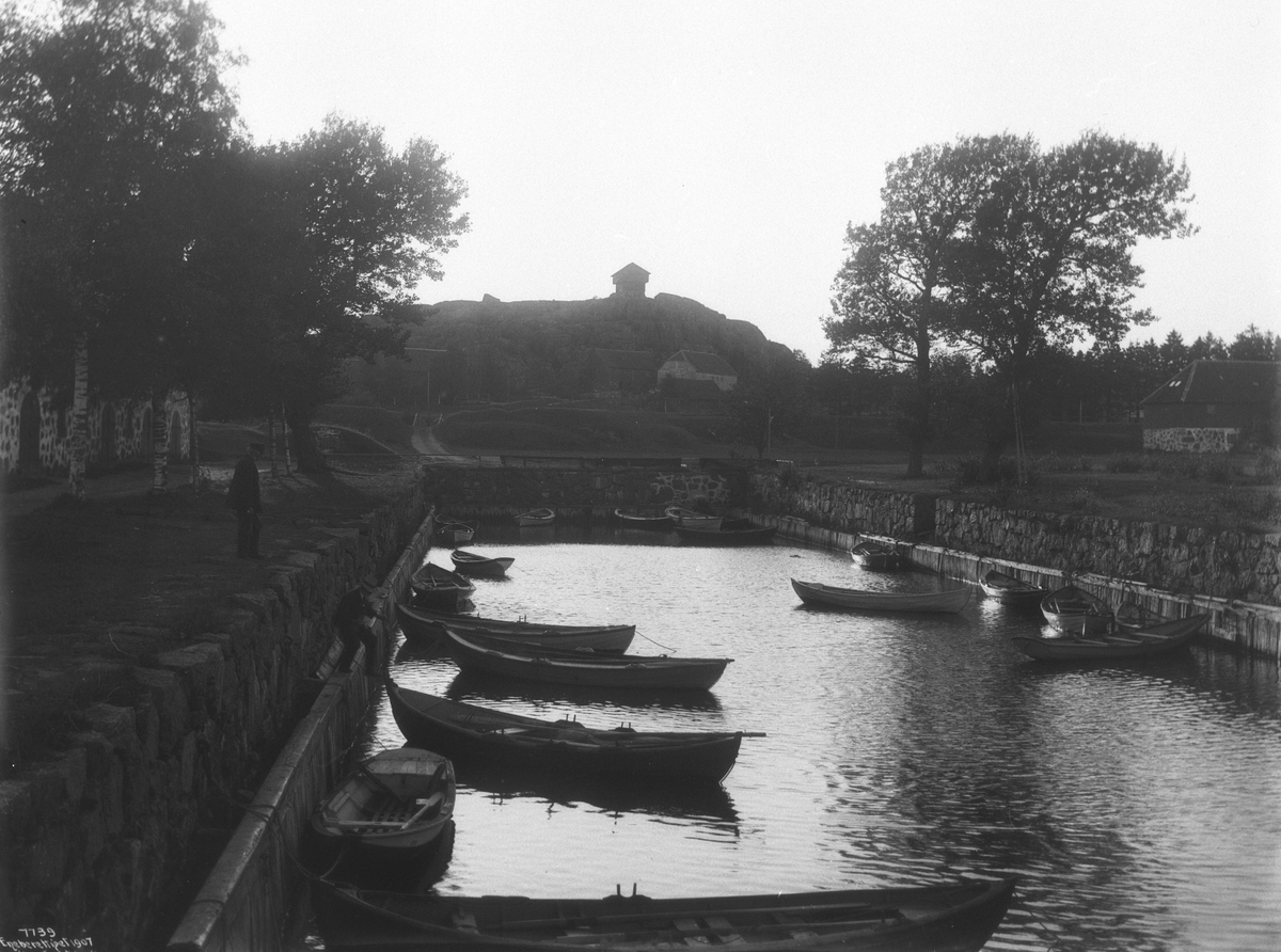 Fortøyde robåter på kanalen på Fredriksvern. Fra midten av 1700-tallet ble stedet marinestasjon med marineverft på fastlandssiden under navnet Fredriksvern (etter kong Frederik 5), som også ble navnet på byen frem til 1930. Stedet ble også befestet med et fort (Fredriksvern). Fotografert i juli 1906.