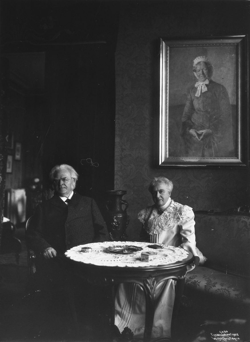 Bjørnstjerne Bjørnson og frue foran maleriet i stuen på Aulestad. Fotografert 17. november 1908.