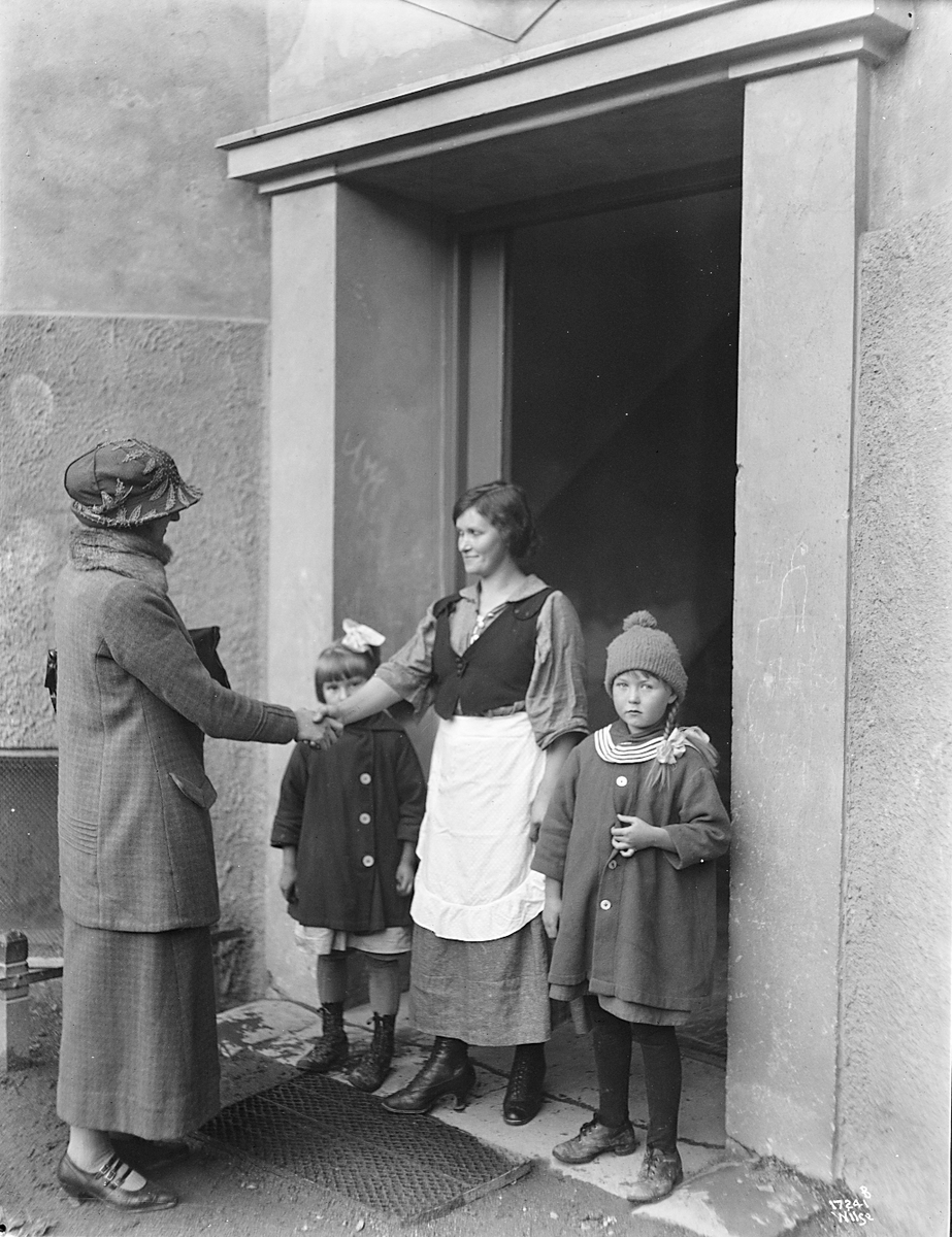 Kvinne fra Hjemmekonsulenten besøker kvinne med to barn i hjemmet. Fotografert 1923.