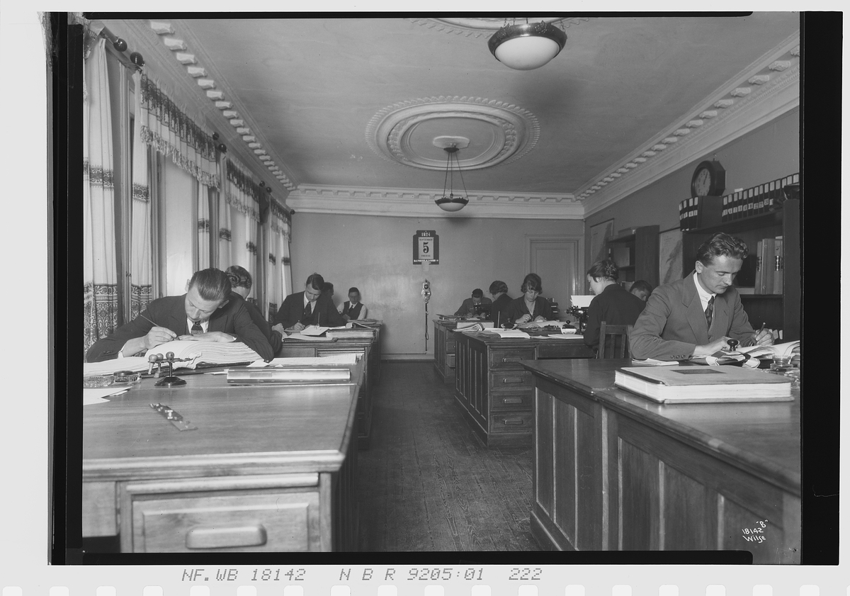 Kvinner og menn sitter sammen på et stort kontor i avd. A, Vinmonopolet. Fotografert 1924