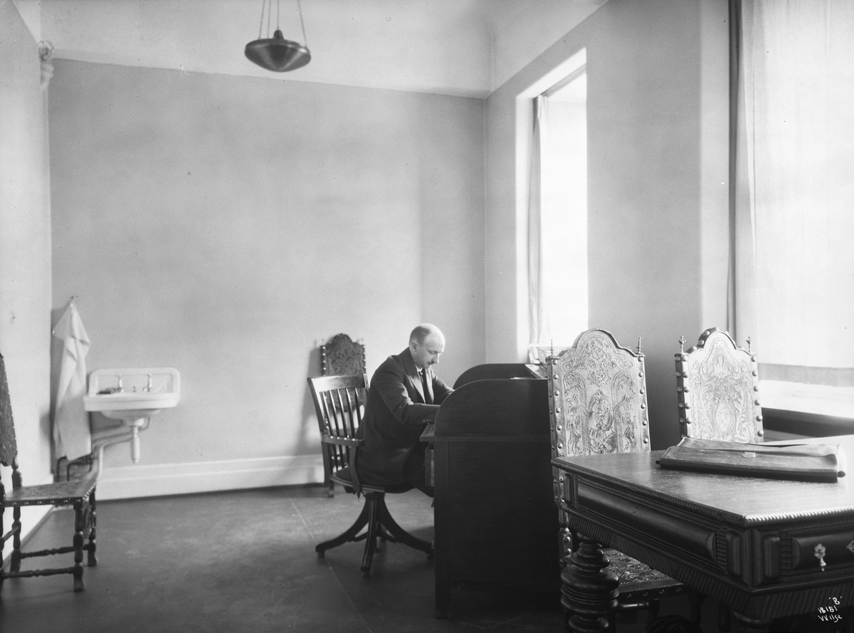 Mann sitter ved skrivebord i et stort rom, Vinmonopolet. Fotografert 1924.