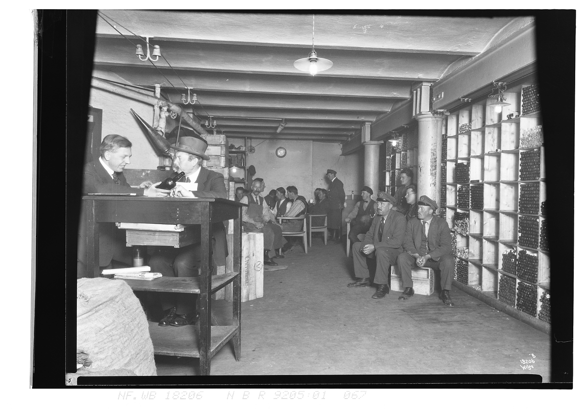 Mange ansatte har pause, vinflasker ligger lagret langs veggen, Vinmonopolet. Fotografert 1924.