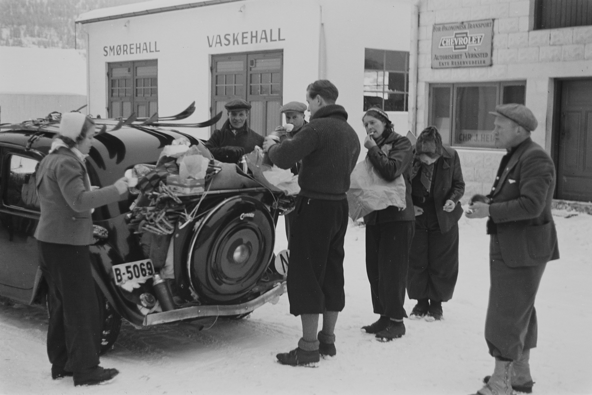Påskefølge tar en pause på bensinstasjonen, tid for mat og drikke.  Skiene er bundet fast på biltaket. Fotografert 1940.