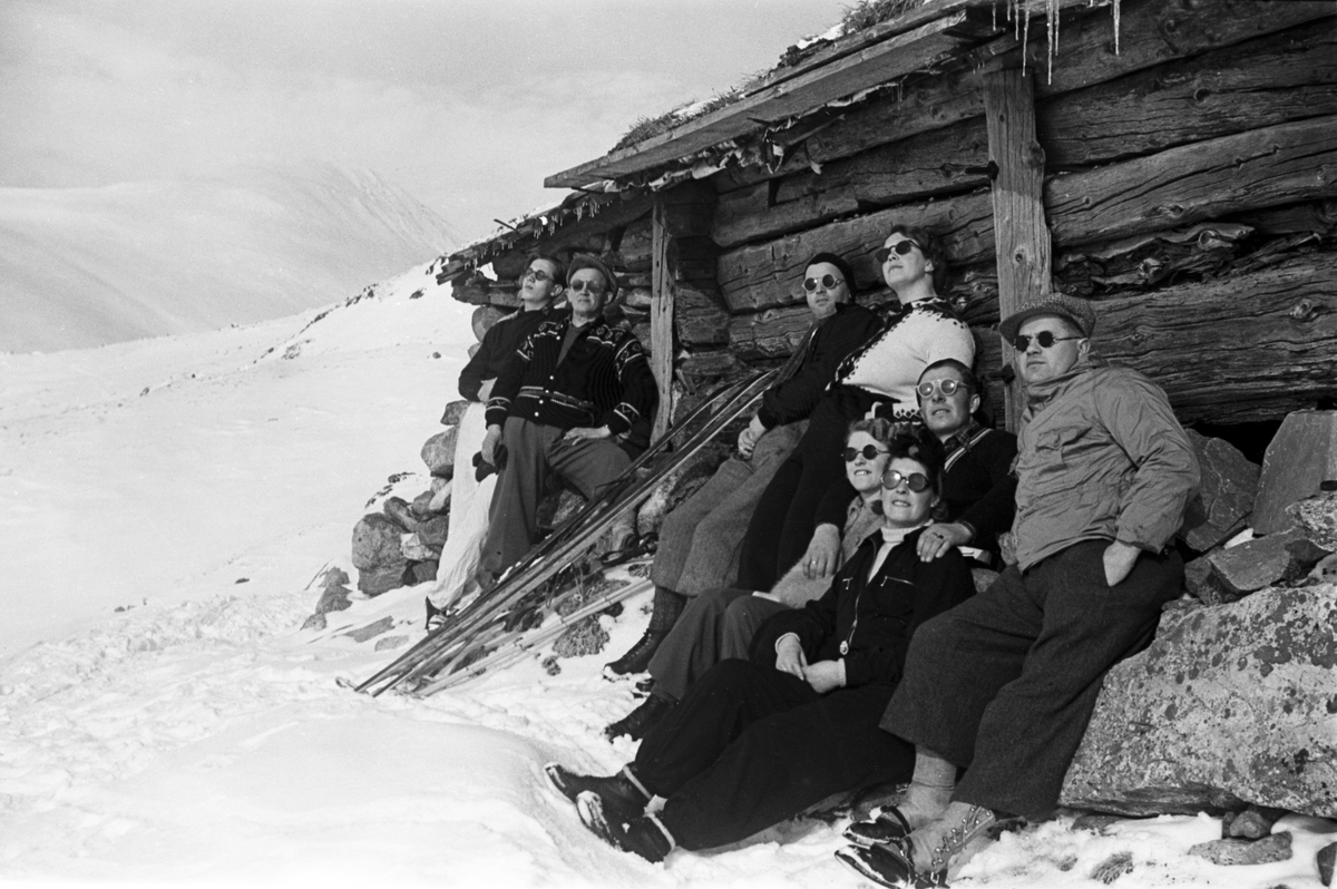 Åtte påsketurister soler seg ved seterbygning i fjellheimen. Fotografert 1940.