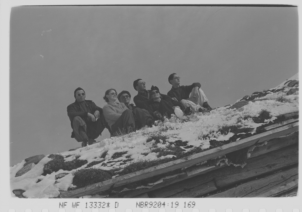 Seks personer soler seg på setertaket i påseken. Fotografert 1940.