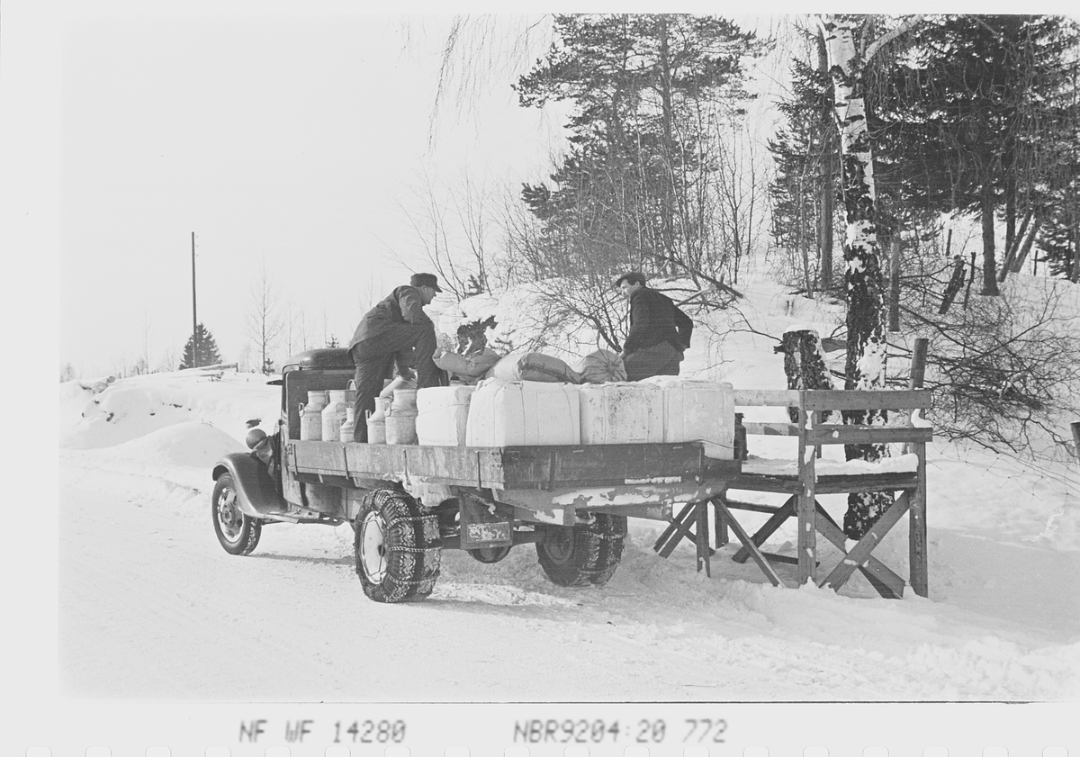 Menn på lasteplanet til melkebilen med melkespann og cellulosefor., ved en melkerampe. Haugsbygda, Ringerike. Fotografert 1941.