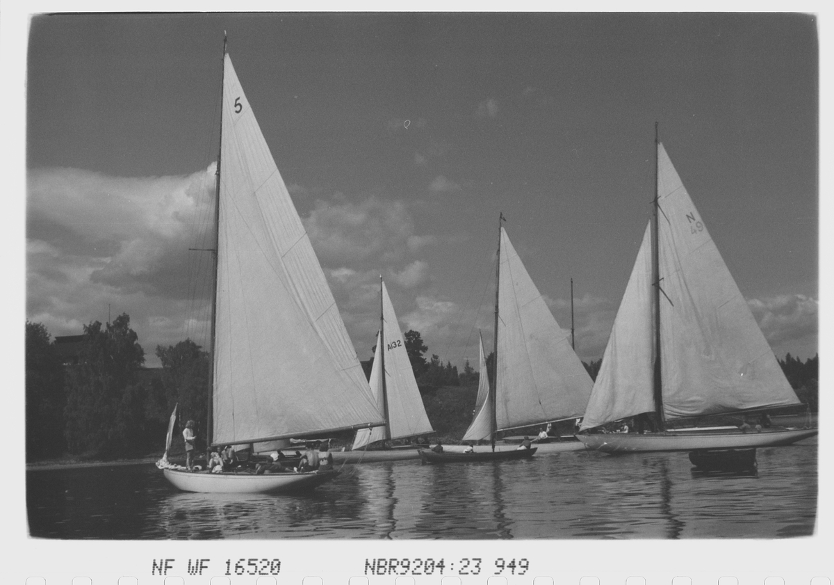 Regatta i vindstille. Blank sjø og store båter i tillegg til mannskapet som ønsker seg litt vind i seilene.