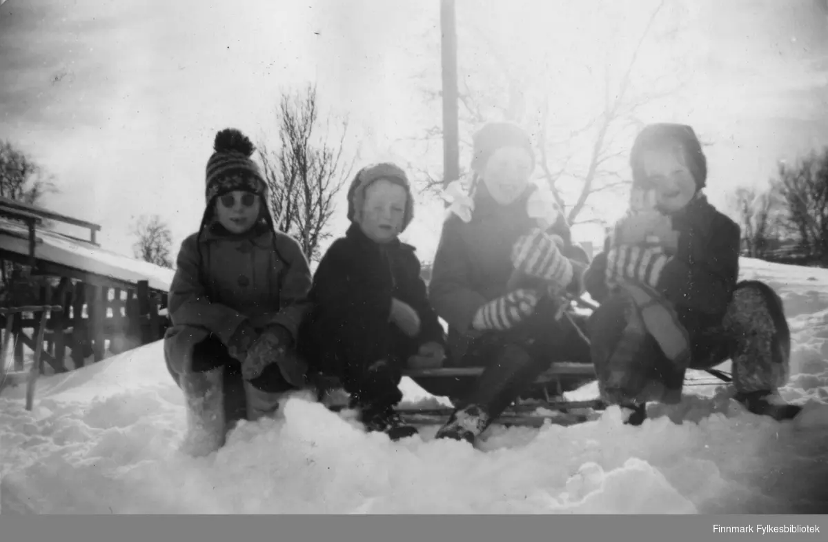 Bilde fra 1957 av fire barn sittende på en rattkjelke tatt utenfor bakeriet i Varangerbotn. Fra venstre Wencke Olsen, Arnfinn Moen, Anne Marie Holien og Svanhild Karlsen.
