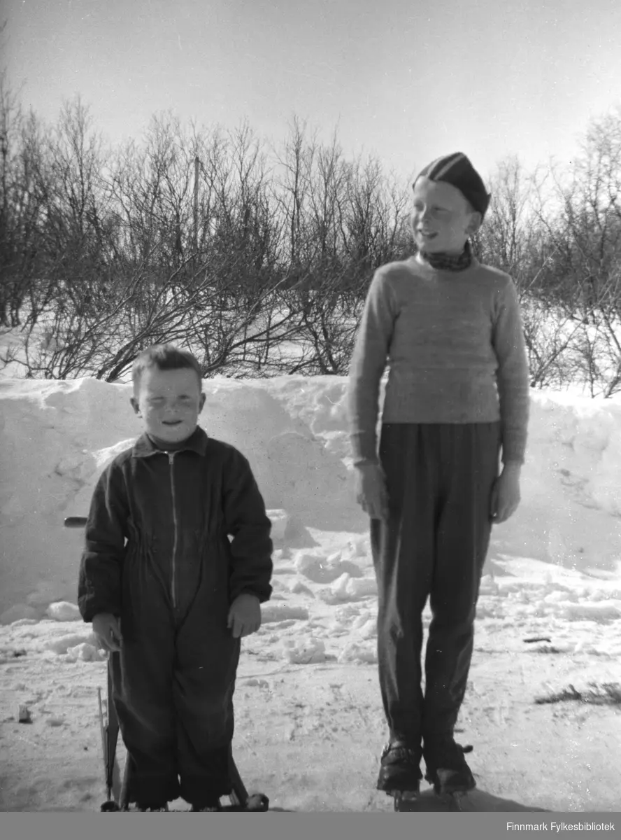 Brødrene Moen, Arnfinn til venstre på spark og Steinar Moen til høyre på skøyter. Bildet tatt på veien utenfor bakeriet i Varangerbotn i 1958.