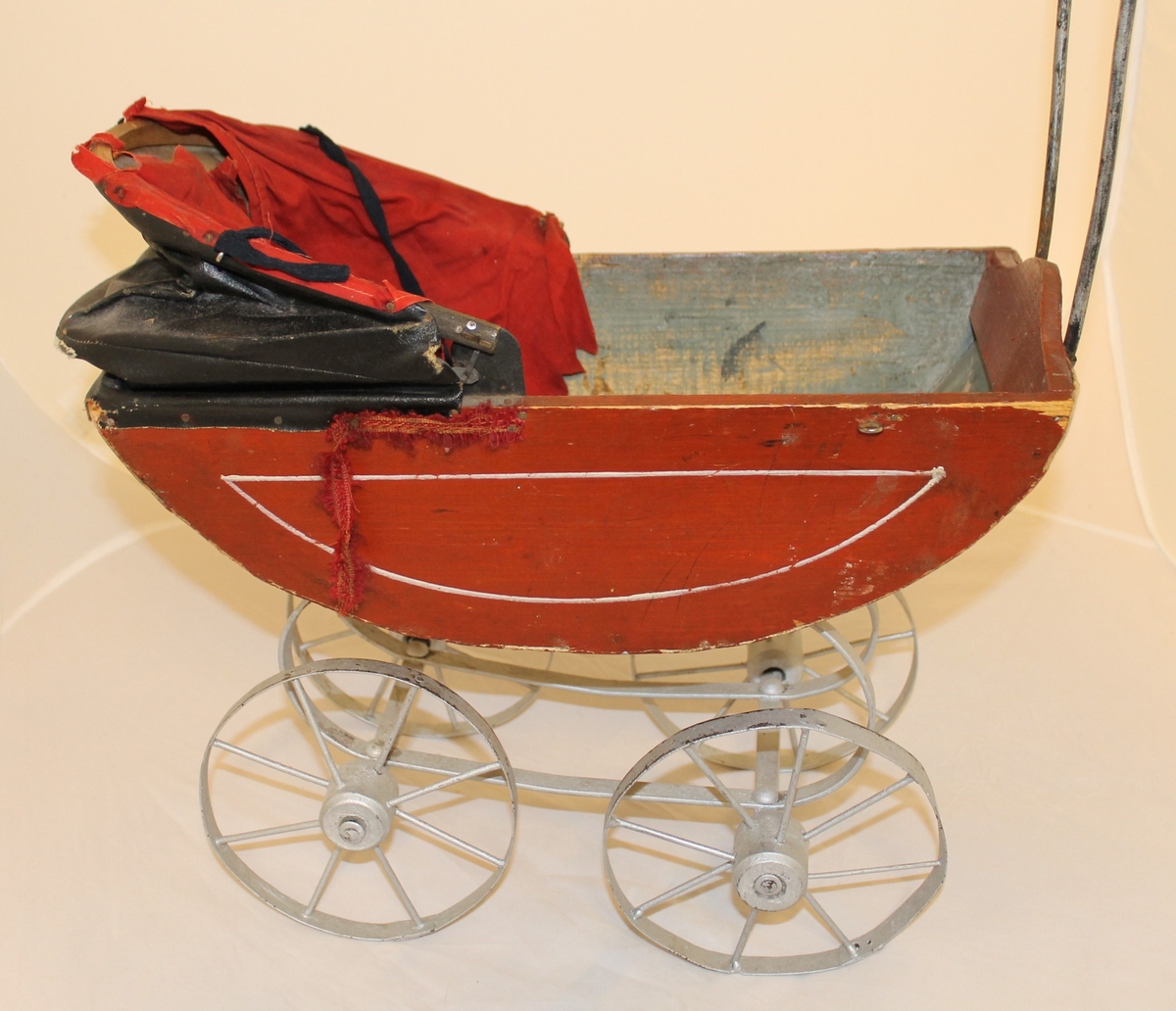 Vognens skrog hviler på fjærer, har 4 hjul og Høy hank med tre håndtak.
Oppi vognen: et putevar og laken med et heklet felt, kaninskinn og sengeteppe.