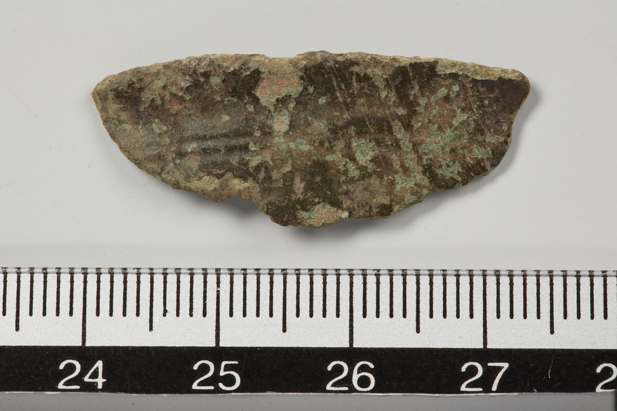 Randfragment av bronsegjenstand, antakelig en krukke eller et beger. Utbøyd munningskant med to dekorlinjer under. Lengde: 3,3 cm.