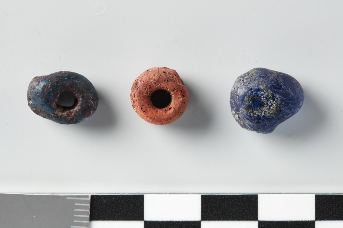 3 runde glassperler, noe deformert av varme: blank blå, std. 1,3 cm, matt blå med røde flekker (sekundære?), std. 1,2 cm, matt mursteinsrød, std. 1,0 cm.