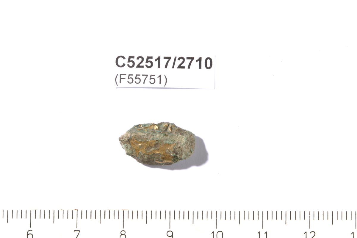 Svært korrodert fragment av et smykke el.l., opprinnelig form uidentifiserbar. En forgylt flate, et opphøyd parti dekket med gullblikk, og et lavere mønstret parti med gullinnlegg.