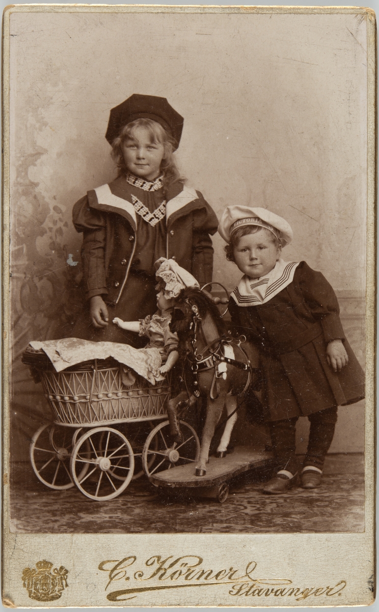Studioportrett av to barn med dukkevogn og lekehest
