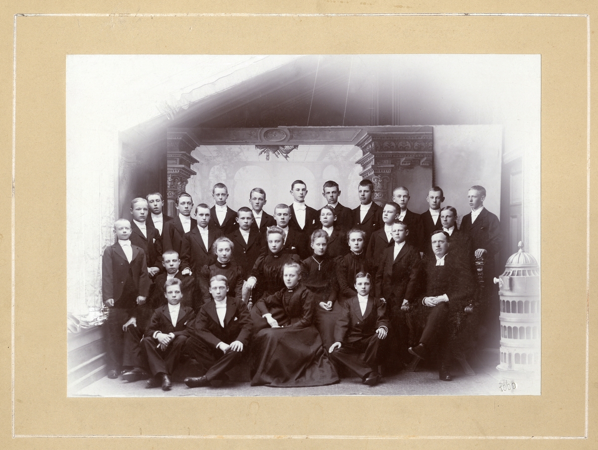 En grupp konfirmander med sin konfirmationspräst (sittande till höger). Årtalet "1899" är instämplat i nhh.
Ateljéfoto.