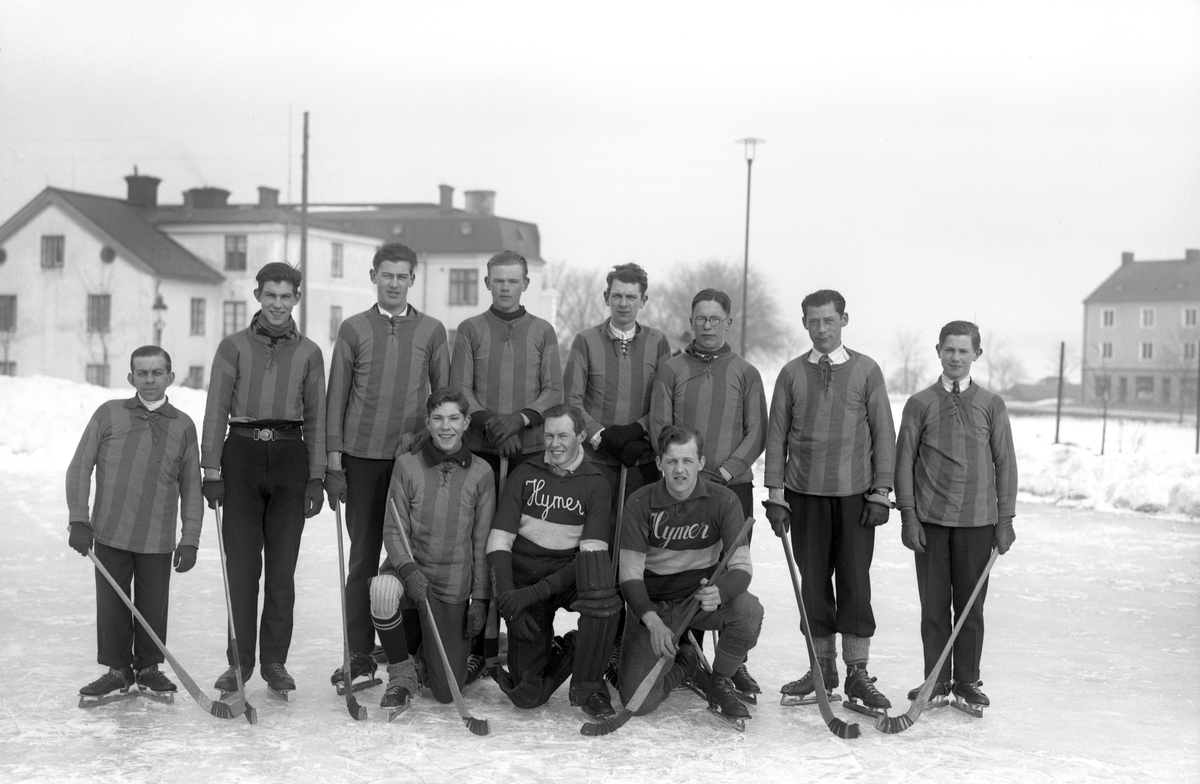 Den linköpingsbaserade cykelklubben Hymer bildades redan 1924 och har sedan dess rönt stora framgångar med ett flertal medaljer på svenska och nordiska mästerskap. För att hålla igång under den sliriga delen av året, spelade man en period tydligtvis även bandy. Här ser vi ett gäng som gjort sig redo för match en vinterdag under 1920-talet. Platsen är Folkskoleseminariets idrottsplats. Vy mot norr med i bakgrund den så kallade Herrgården (Västanågatan 3A) invid det så kallade Elgstrandska huset (Västanågatan 3C). Till höger ses del av affärs- och bostadshuset på adressen Hunnbergsgatan 41.