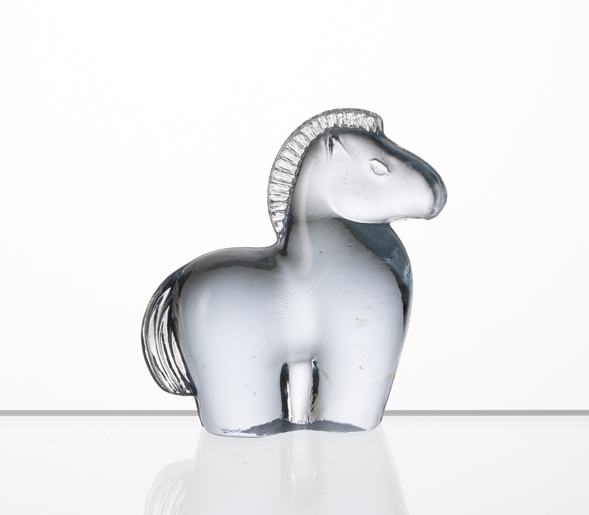 Formgiven av Kjell Blomberg. Mindre figuring i svagt blåtonat glas, föreställande en häst.