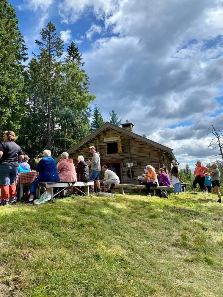 Liv og røre på Skålbergsætra. Mennesker i fargerike klær er samlet rundt sætra. Fint sommervær.