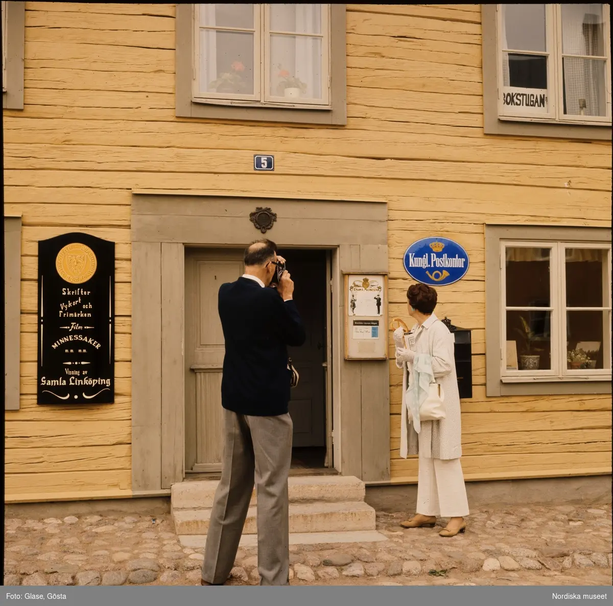 Gamla Linköping. En man fotograferar en kvinna framför ett postkontor.
