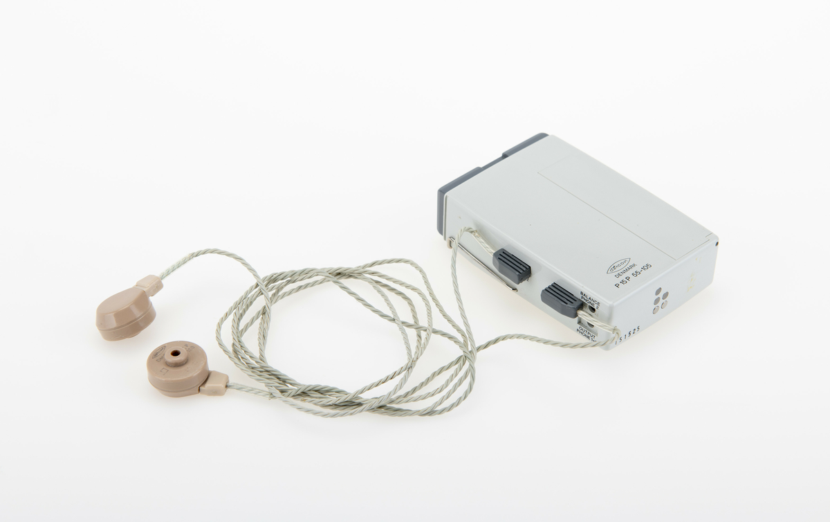 Høreapparat i grå plast, med ledning til øreplugger. Høreplugger inkludert.