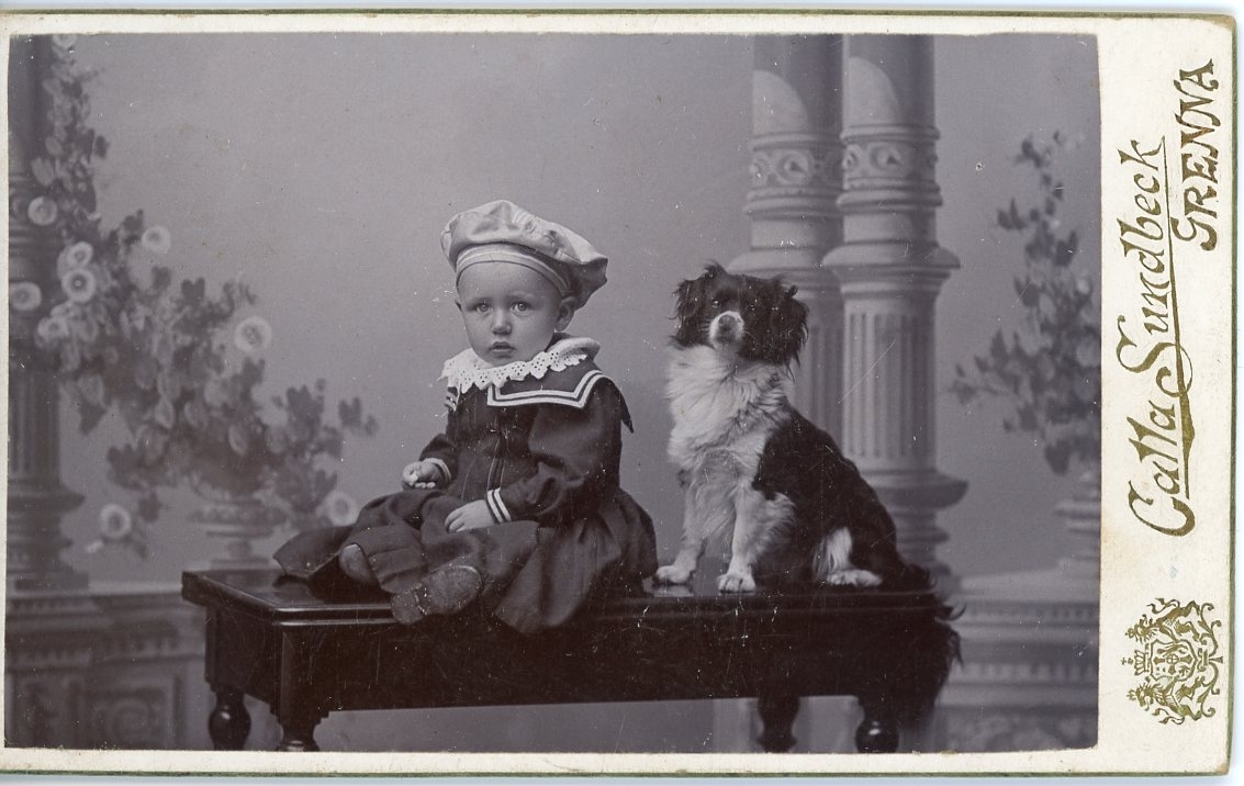 Kabinettsfotografi av ett späbarn och en hund som sitter på ett bord.