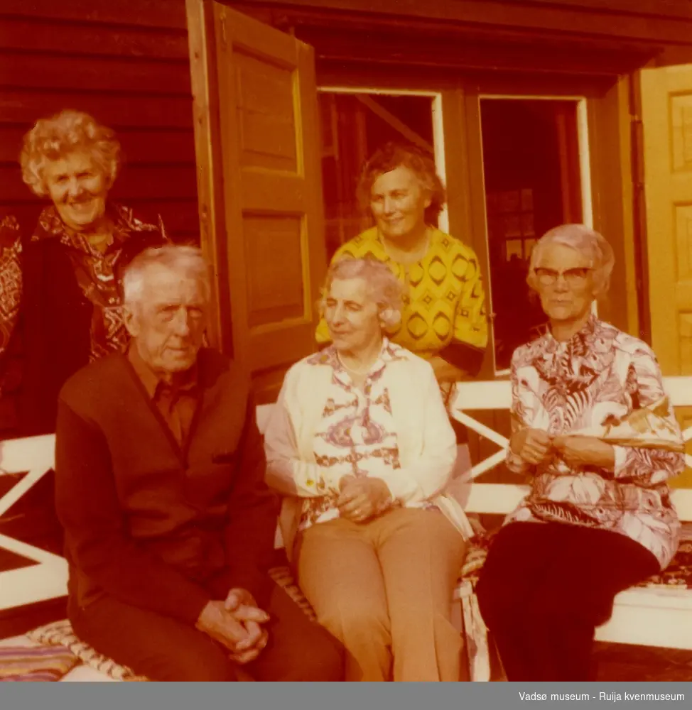 Gruppe mennesker fotografert på trappen utenfor Esbensens hytte i Jakobselv, Vadsø kommune.  Fra venstre foran:  Ingrid Skogsholm, Bjarne Skogsholm. Fra venstre bak: Ella Esbensen og Lilly Simonsen. ca 1970 tallet.