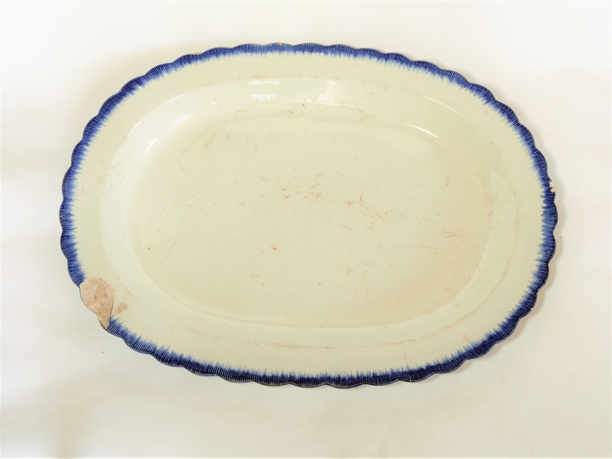 Serveringsfat med oval form med tunget ytterkant.
Hvit bunn med blå stripebord ytterst.
Se også FFB 534, 513, 514
Dekorteknikk: Malt
Se opplysn. om fa,: "English Pottery & Porcelain" s. 110